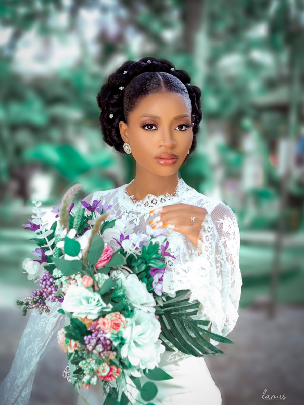 Portrait Of A Bride With An Ornate Hairstyle And White Lace Gown Holding A Lush Green And White Floral Bouquet.
